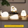 Several cute LED night lights shaped like animals and fruit are displayed on a wooden surface, with books and a plant in the background. Produktbild-Vorschau