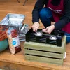 A person is shown preparing a portable stove on a wooden deck. Produktbild-Vorschau