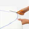Hands cutting a white fabric with blue markings using orange-handled scissors. Produktbild-Vorschau