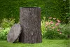 A rain barrel designed to look like a tree trunk, placed in a garden setting next to pink flowers. Produktbild-Vorschau