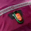 A close-up of a reflective strip with the brand name 'coocazoo' and a small red LED light attached to a purple fabric. Podgląd zdjęcia produktu