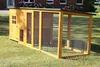 A wooden chicken coop with an attached run is situated on a grassy lawn in front of a brick house. Produktbild-Vorschau