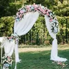 A wedding arch decorated with flowers and draped with white fabric, set up outdoors on a lawn. Podgląd zdjęcia produktu