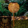 A solar-powered garden light with a decorative metal sphere is shown in a garden setting at dusk. Náhled obrázku produktu