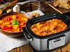 A slow cooker filled with stew is placed next to a bowl of the same stew, on a wooden table. Produktbild-Vorschau