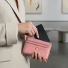 A person is holding a pink wallet and putting a black card holder into it. Produktbild-Vorschau