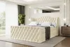 A luxurious beige velvet boxspring bed with a tufted headboard and footboard is set up in a well-lit bedroom with sheer curtains and a large mirror reflecting the ceiling. Produktbild-Vorschau