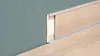 A close-up view of a white PVC skirting board with a light wood grain effect, installed along a teal wall and light wood floor. Produktbild-Vorschau