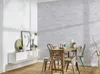 A dining area with a table and chairs set against a brick wall, with a shelf displaying decorative items on the opposite wall. Náhled obrázku produktu