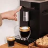 A hand is pressing a button on a coffee machine, with two cups of coffee in the foreground and a bowl of sugar cubes in the background. Produktbild-Vorschau