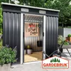 A dark gray metal garden shed with its sliding door open, revealing organized tools and storage inside. The shed is situated outdoors on a paved patio, with greenery and a wheelbarrow visible in the background. A watering can and a potted plant are in the  Produktbild-Vorschau