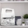 A white hand mixer with its attachments stored in a clear plastic container, displayed on a shelf with decorative items. Produktbild-Vorschau