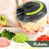A person is holding a manual food chopper with chopped ingredients in bowls in the foreground. Produktbild-Vorschau