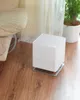 A white humidifier sits on a wooden floor next to a chair and a plant. Produktbild-Vorschau