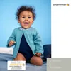 A baby wearing a blue knitted cardigan and romper against a blue background. Produktbild-Vorschau