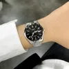 A person's wrist wearing a silver watch with a black dial. Náhľad obrázku produktu