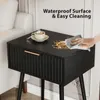 A hand is wiping a spill off a black nightstand with a gold drawer pull. A cup of coffee is on the nightstand. Produktbild-Vorschau