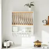 A white kitchen shelf unit with wooden plate dividers, holding white plates. Below are white bowls, glasses, and mugs hanging from hooks. A toaster and faucet are visible on the counter. Produktbild-Vorschau