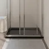A close-up view of a black rectangular shower tray with a silver frame, set against a tiled wall and a light-colored rug on the floor. Produktbild-Vorschau