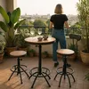 A woman stands on a balcony overlooking a city, with a bar table and stools set up. Produktbild-Vorschau