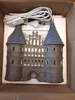 A ceramic lighthouse-shaped decoration with a power cord and plug sits inside a cardboard box lined with white foam packaging. Produktbild-Vorschau