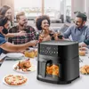 A group of friends are gathered around a table, enjoying a meal and drinks, with an air fryer prominently displayed. Produktbild-Vorschau