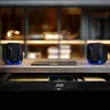 Two compact speakers and a laptop on a desk, with an open drawer below. Náhľad obrázku produktu