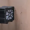 A black storage organizer with clear compartments is being held up against a wooden wall. Produktbild-Vorschau