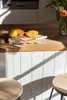 A kitchen counter with a cutting board, fruit, and knives, with stools in the foreground. Anteprima dell’immagine prodotto