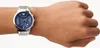 A close-up shot of a man's wrist wearing a silver Emporio Armani watch with a blue dial. Náhľad obrázku produktu
