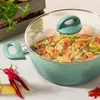 A teal pot filled with zucchini noodles, shrimp, and lemon slices, with red chili peppers and spices in the foreground. Produktbild-Vorschau
