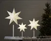 Three illuminated star-shaped lamps are displayed in front of a wooden wall, with a decorated Christmas tree in the background. Podgląd zdjęcia produktu