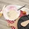 A whisk in a bowl of batter, with baking ingredients and tools around it. Produktbild-Vorschau