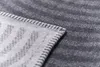 A close-up view of a gray blanket with a zigzag pattern, showing the stitched edge. Produktbild-Vorschau