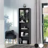 A tall, black bookshelf filled with decorative items and books, placed next to a window with light gray curtains. A dark gray ottoman with a fluffy cushion sits in front of the bookshelf. Náhled obrázku produktu