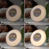A collage of four images showing a sunrise alarm clock with a person sleeping in the background. Each image shows the clock at a different time and brightness level. Produktbild-Vorschau