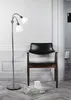 A modern interior scene featuring a black leather armchair, a floor lamp, and a stack of magazines with a mug on top. Náhled obrázku produktu
