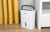 A white dehumidifier is placed on a wooden floor next to a white cabinet and a yellow curtain. Náhľad obrázku produktu