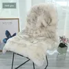 A sheepskin rug is draped over a chair in a room with a framed picture and a plant. Produktbild-Vorschau