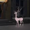 A lighted reindeer decoration is placed on a snowy ground in front of a house at night. Podgląd zdjęcia produktu