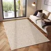 A cream-colored rug is laid out on a wooden floor in a living room setting, with a sofa and a floor lamp visible in the background. Náhled obrázku produktu
