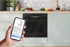A hand holding a smartphone in front of a modern kitchen oven. Anteprima dell’immagine prodotto