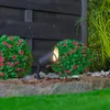 A black outdoor spotlight illuminates a garden setting with artificial bushes and a wooden fence. Náhľad obrázku produktu