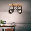 A ceiling light fixture with two adjustable spotlights mounted on a wooden base, shown in a room setting with a shelf and decorative items. Produktbild-Vorschau