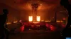 A dimly lit, eerie room with a central pool of red liquid and two silhouetted figures. Produktbild-Vorschau
