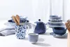 A collection of blue and white ceramic tableware, including a teapot, mugs, and bowls, arranged on a white surface. Produktbild-Vorschau