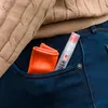 A close-up shot of a pocket in blue jeans, containing a folded orange cloth and a transparent spray bottle with a red cap. Náhled obrázku produktu