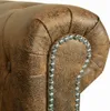 A close-up view of the corner of a brown Chesterfield sofa, showing tufted detailing and decorative silver studs. Náhled obrázku produktu