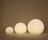 Three illuminated spherical lamps of varying sizes are arranged in a row against a plain, light brown background. Produktbild-Vorschau