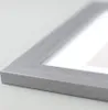 A close-up shot of the corner of a silver picture frame, showing the texture of the frame and a hint of the white matting and artwork inside. Produktbild-Vorschau